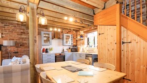 A cozy kitchen with wooden beams, a dining table, and a brick wall. - The Dairy Barn (Fakenham)