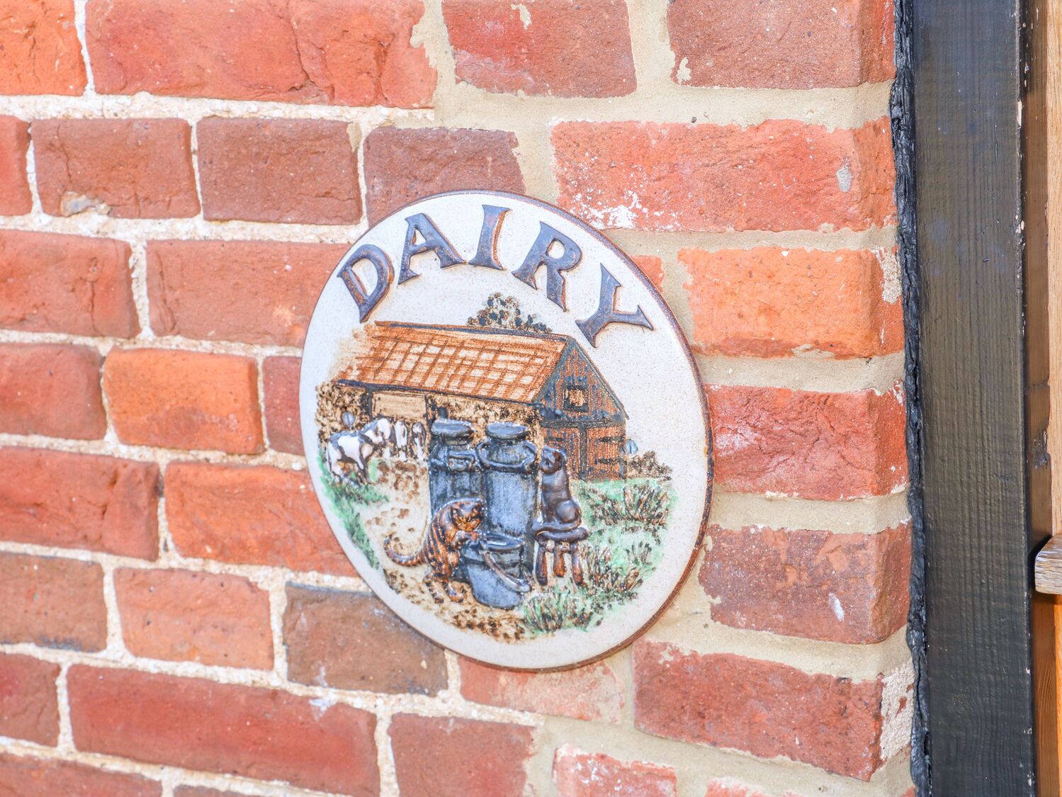 A circular sign with the word "DAIRY" and a depiction of a barn and cows on a brick wall.