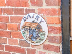 Un letrero circular con la palabra 'DAIRY' y una representación de un granero y vacas sobre un muro de ladrillos.