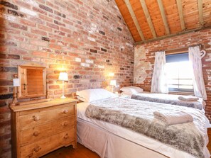 Un dormitorio con dos camas, mesitas de noche de madera, un aparador y una pared de ladrillo.