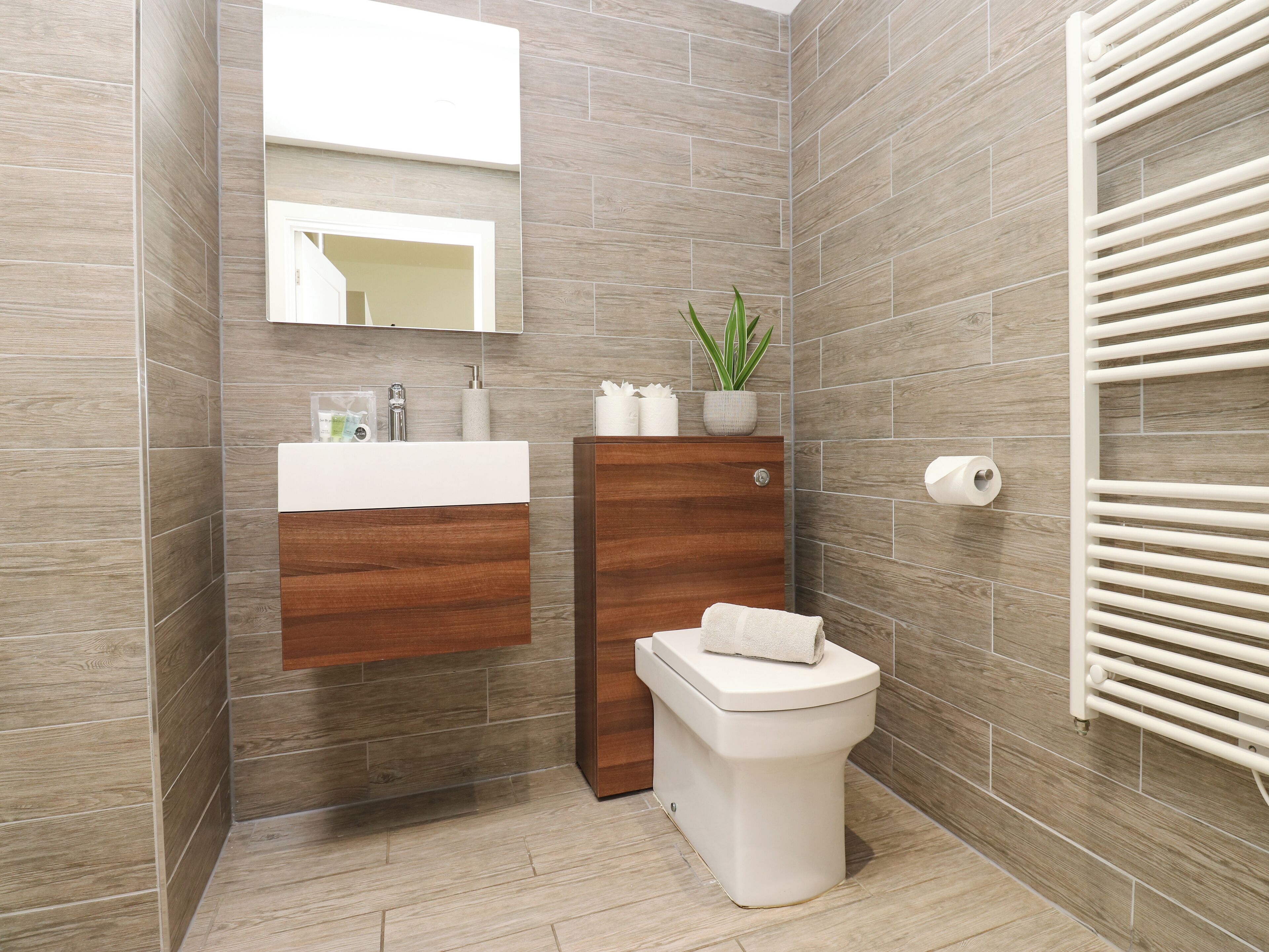 A modern bathroom with a wooden vanity, a toilet, and a towel rack.