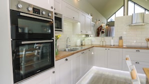 A modern kitchen with white cabinetry, stainless steel appliances, and a wooden countertop. - Restharrow Lodge (Bamburgh)