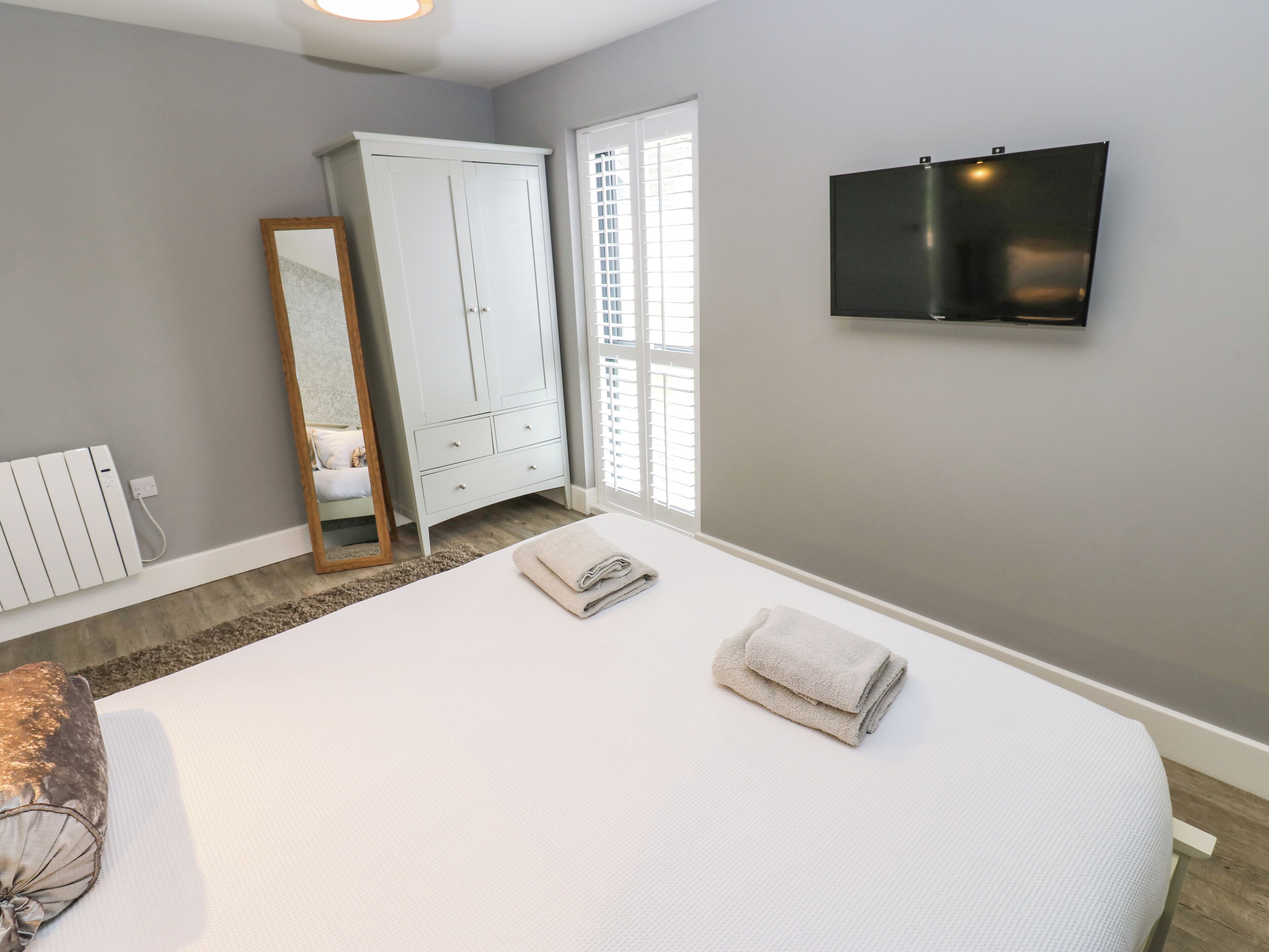 A bedroom with a large bed, a wardrobe, a mirror, a TV, and a radiator.