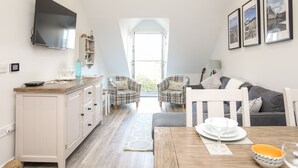 Una cocina moderna con comedor, televisor montado en la pared y un amplio ventanal que proporciona luz natural.