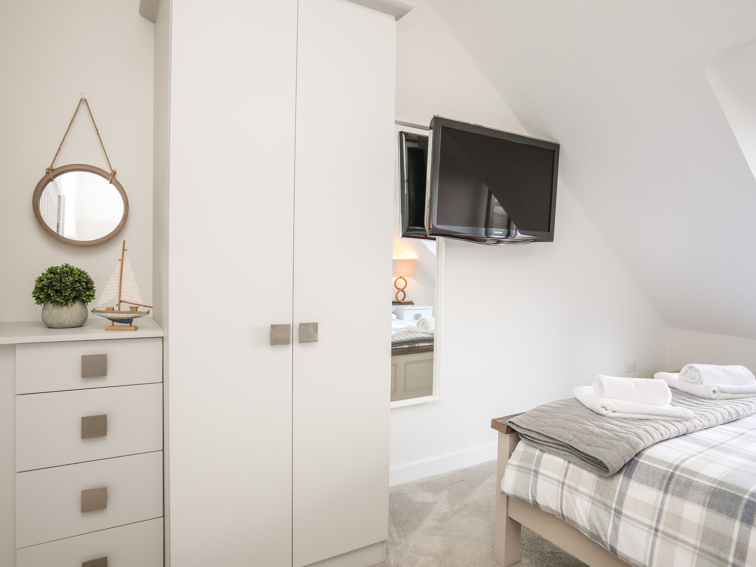 A bedroom with a bed, a TV mounted on the wall, a wardrobe, a mirror, and a small potted plant.