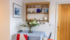 A cozy room with a dining table set for two, a vase of flowers, a shelf with kitchenware, and a wooden door. - Wallerthwaite Barn Cottage (Harrogate)