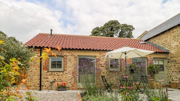 A stone building with a red-tiled roof, a small garden with pebbles and plants, and a white umbrella. - Wallerthwaite Barn Cottage (Harrogate)