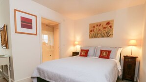 A bedroom with a large bed, two bedside lamps, a painting on the wall, and a door leading to another room. - Wallerthwaite Barn Cottage (Harrogate)
