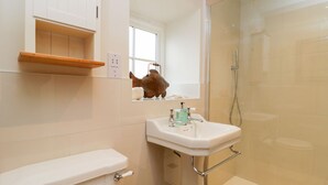 A bathroom with a toilet, sink, shower, and a shelf with a fish decoration. - Wallerthwaite Barn Cottage (Harrogate)
