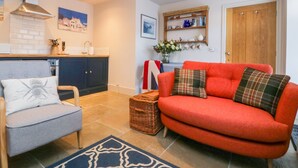 A cozy living room with a red sofa, a grey armchair, and a blue patterned rug. - Wallerthwaite Barn Cottage (Harrogate)