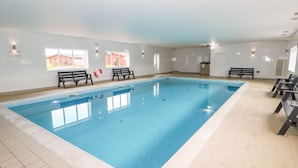 Une piscine intérieure à l’eau d’un bleu limpide, avec un sol carrelé et des bancs le long des parois.