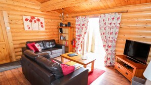 L’intérieur d’une cabane en rondins, avec un canapé en cuir, une table basse en bois, un téléviseur et une bibliothèque.