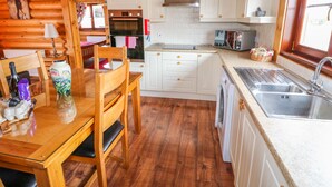 L’intérieur chaleureux d’un chalet en bois comprend une table à manger en bois, des chaises, une cuisine avec des meubles blancs, un four à micro-ondes et un lave-linge.