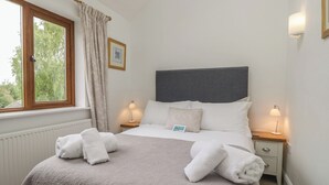 A neatly made bed with a headboard, two bedside lamps, a window with curtains, and a radiator.