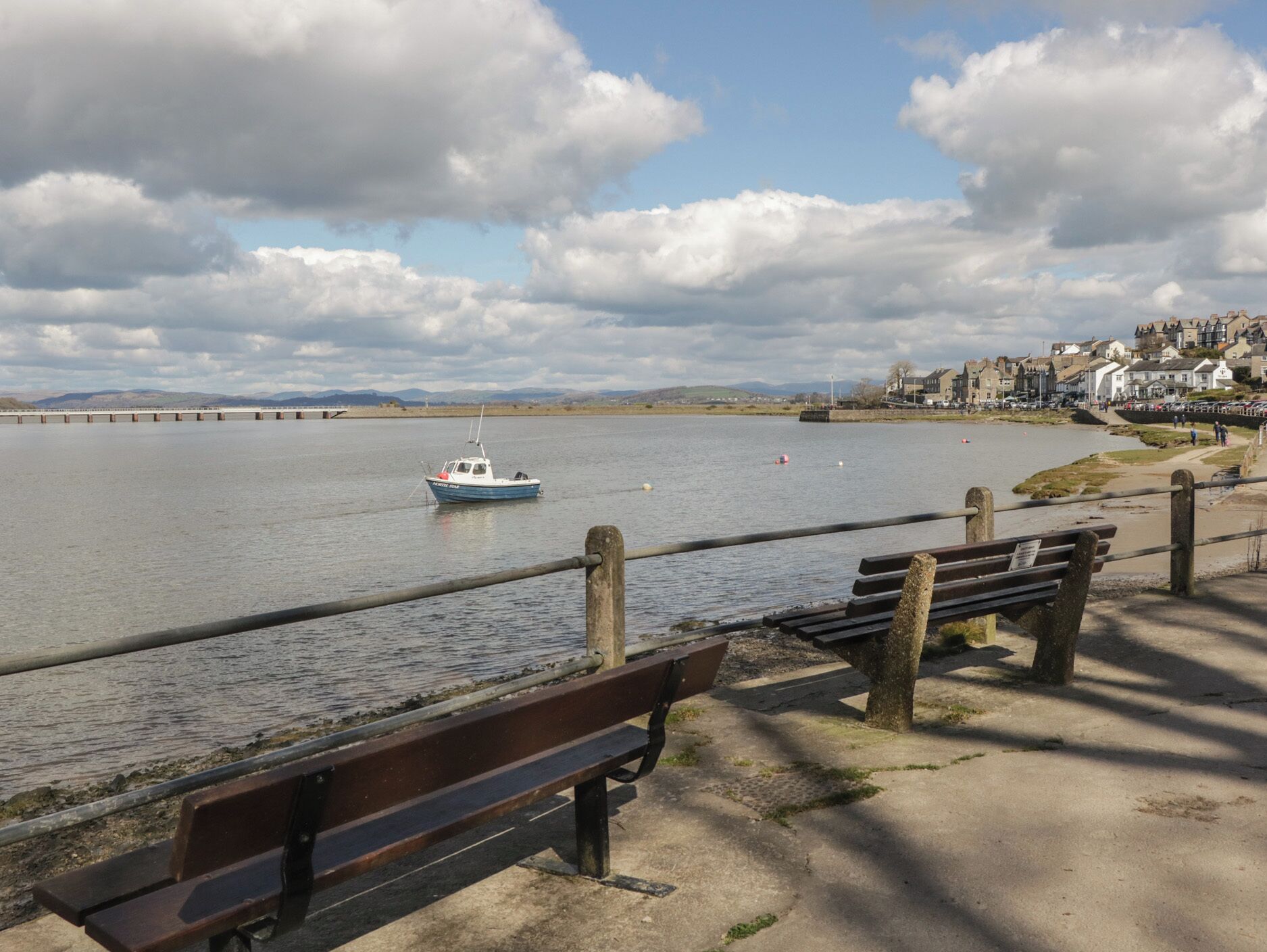 A waterfront view with a bench, a boat, and a distant bridge.