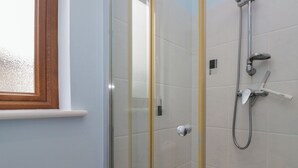 A glass-enclosed shower area with a handheld showerhead and a wall-mounted faucet.