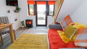 Een gezellige woonkamer met een bank, een tafel met croissants, een open haard en een aan de muur bevestigde televisie.