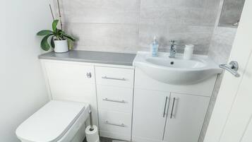 Un baño pequeño con inodoro blanco, lavamanos con espejo y una planta pequeña en maceta.