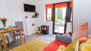 Een gezellige woonkamer met een bank, een eethoek met een tafel en stoelen, een aan de muur bevestigde televisie en een open haard.