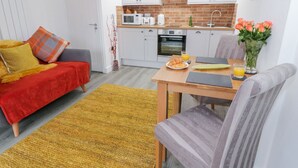 Een knus woongedeelte met een kitchenette, een bank, een eettafel en een stoel.