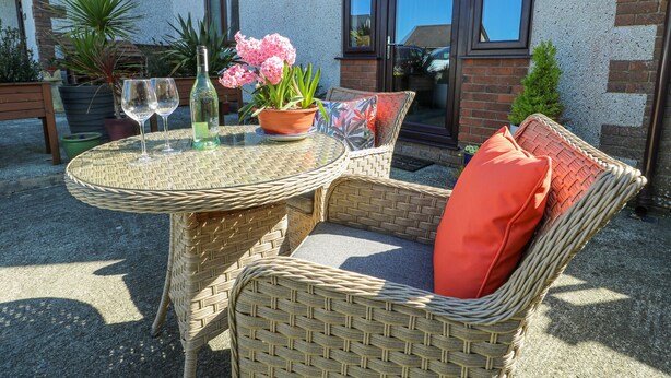 Een terras met rieten meubels, een tafel met een bloempot en een fles.