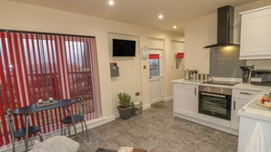 Een praktische keuken met moderne apparaten, een eetgedeelte met een tafel en stoelen, en een gezellige zithoek met een bank en kussens.