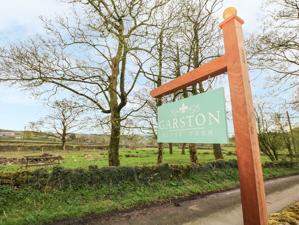 Un panneau indiquant l’emplacement de la ferme Garston House, avec un paysage rural en arrière-plan.