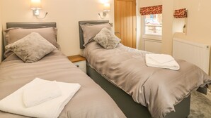 Een hotelkamer met twee bedden, elk met hoofdeinde, nachtkastjes en lampen. Er is een raam met uitzicht.