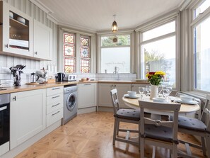 A modern kitchen with white cabinetry, a built-in washing machine, and a dining area with a round table and chairs. - Bayview Terrace (Lynton)