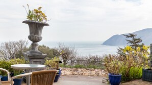 An outdoor patio with stone flooring, wicker chairs, a table, and potted plants. - Bayview Terrace (Lynton)