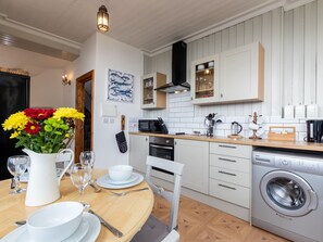 A modern kitchen with white cabinetry, a wooden countertop, a built-in washing machine, and a dining area with a table set for two. - Bayview Terrace (Lynton)