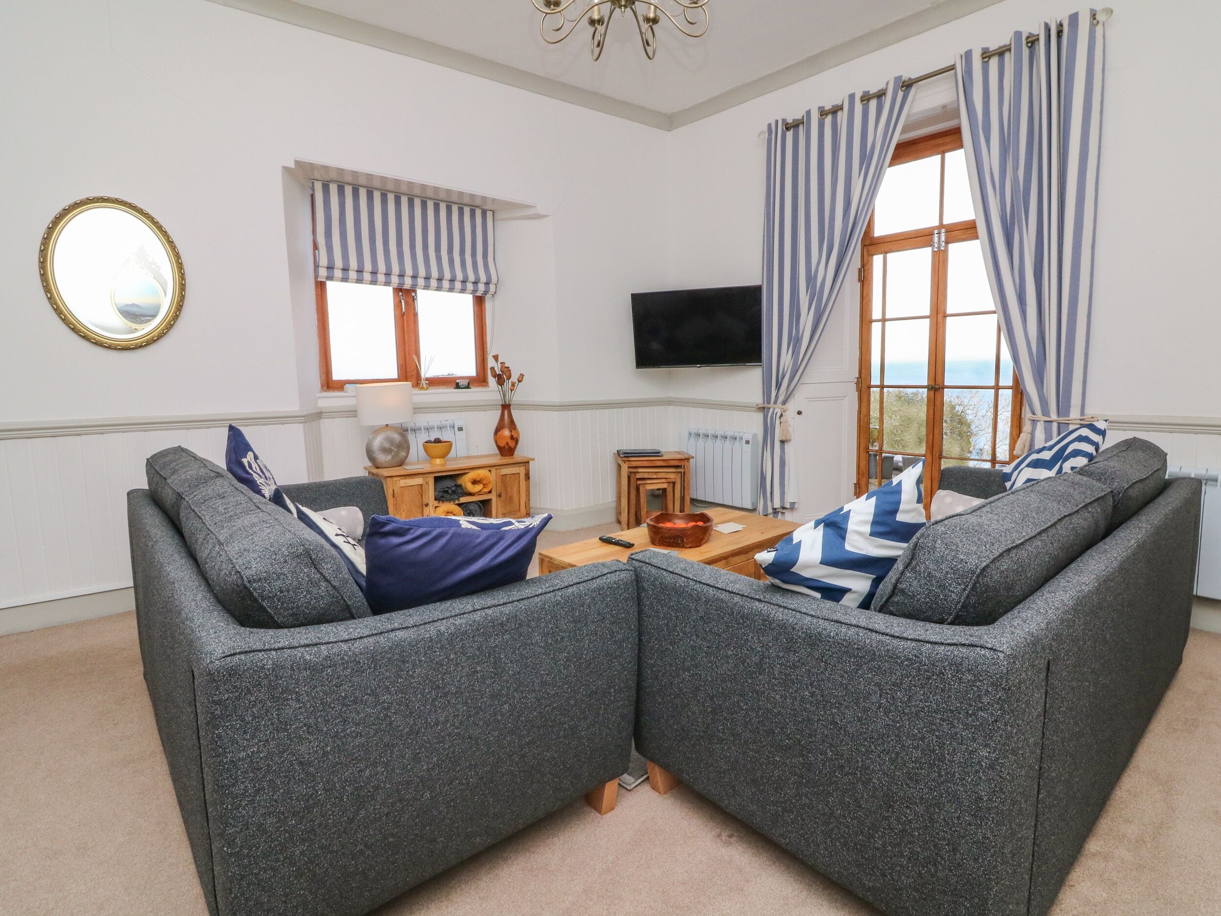 A living room with two grey sofas, a wooden side table, a TV, and a window with striped curtains.