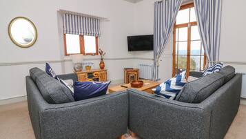 A living room with two grey sofas, a wooden side table, a TV, and a window with striped curtains.