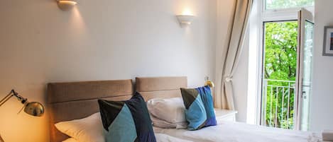 Cama doble con dos almohadas, lámpara de noche y ventana con cortinas.