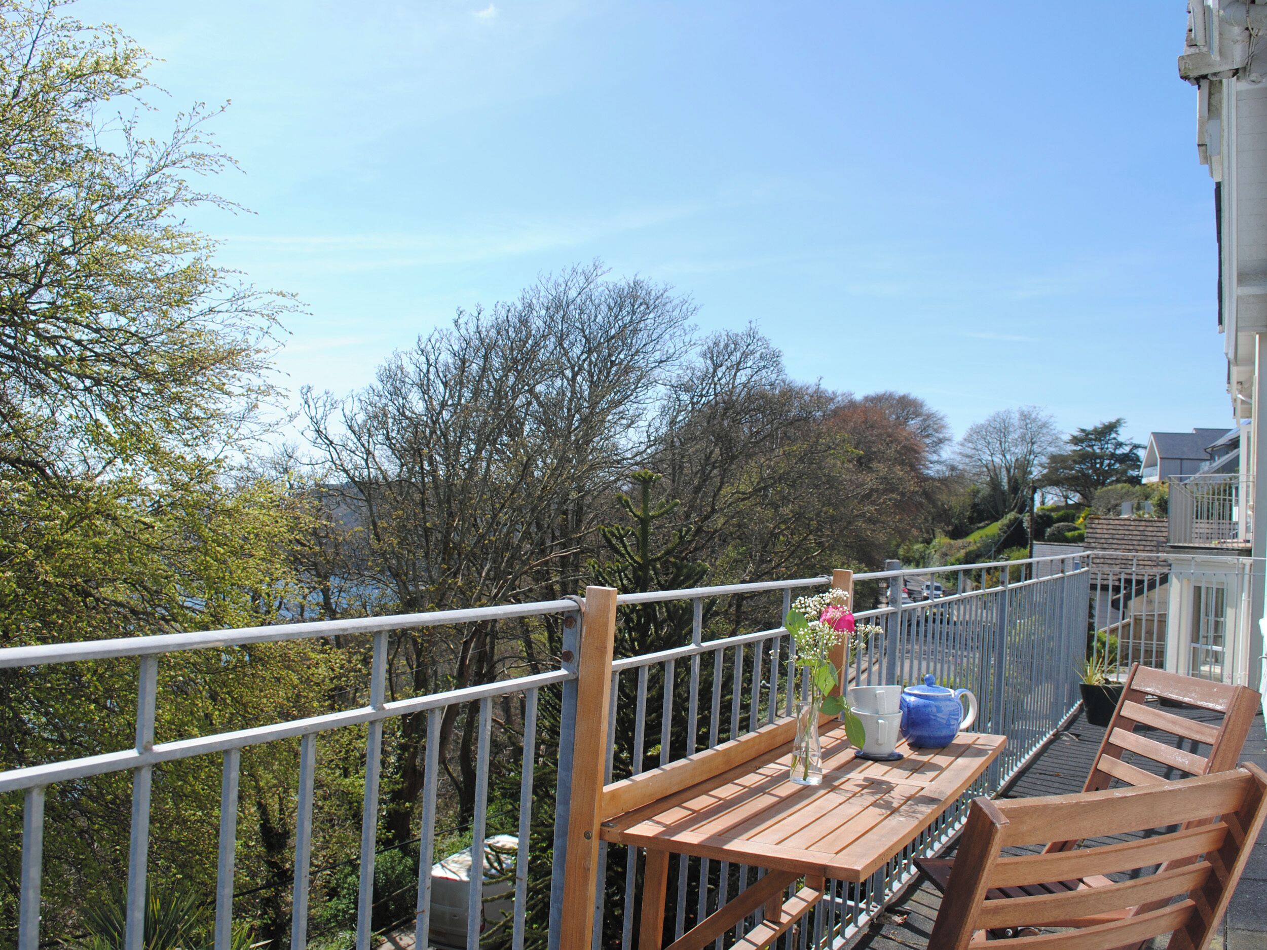 Een balkon met een houten tafel, een stoel en een plant in een pot.