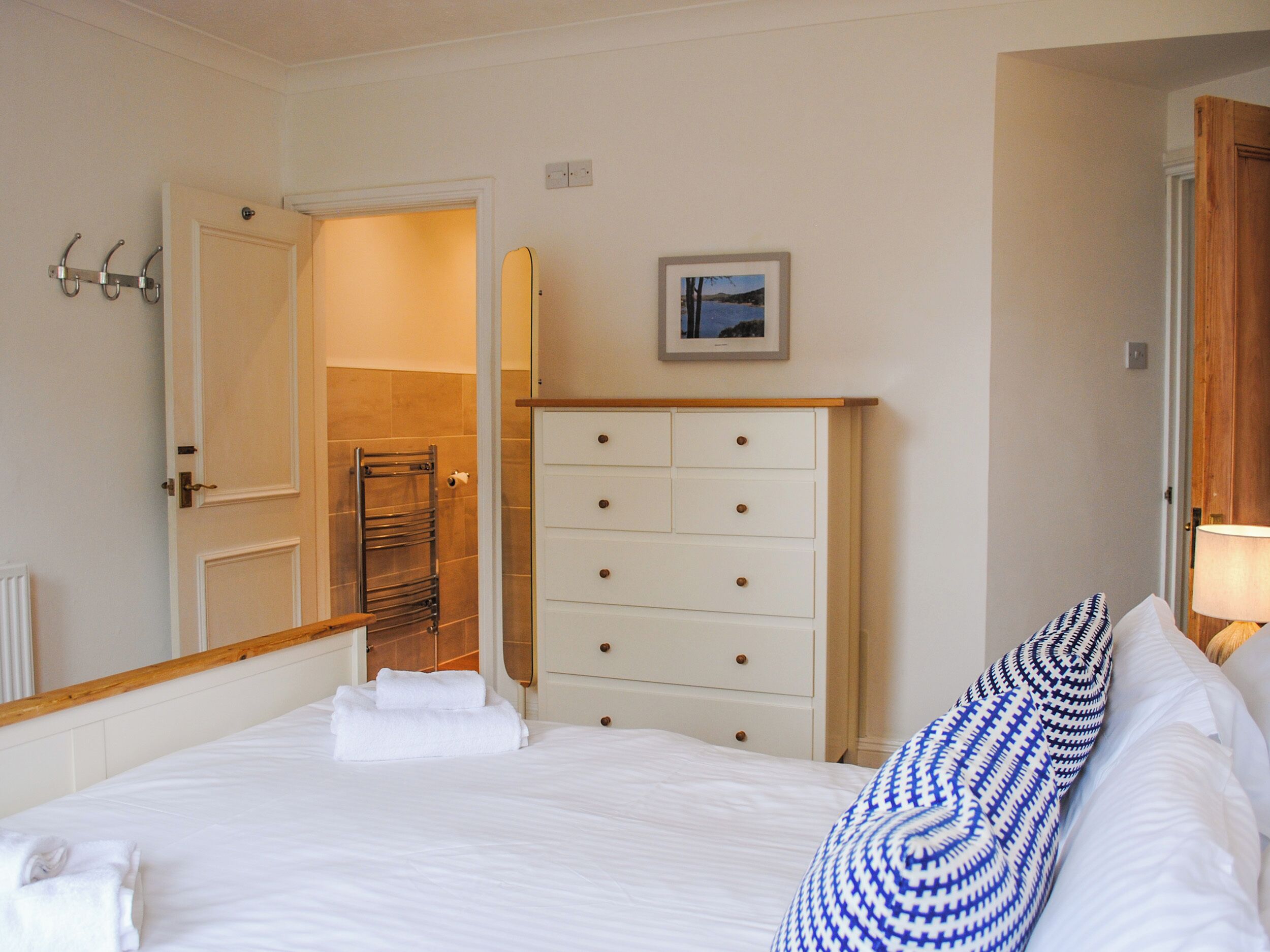 Habitación de hotel con cama, cómoda, espejo, toalla y un cuadro en la pared.