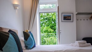 A bedroom with a bed, pillows, a window, and a door leading to a balcony. - 3 Melbury (Salcombe)