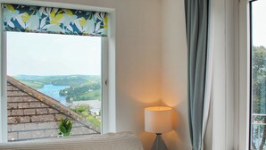 A room with a bed, a window with a view of a landscape, a lamp, and a curtain. - 3 Melbury (Salcombe)