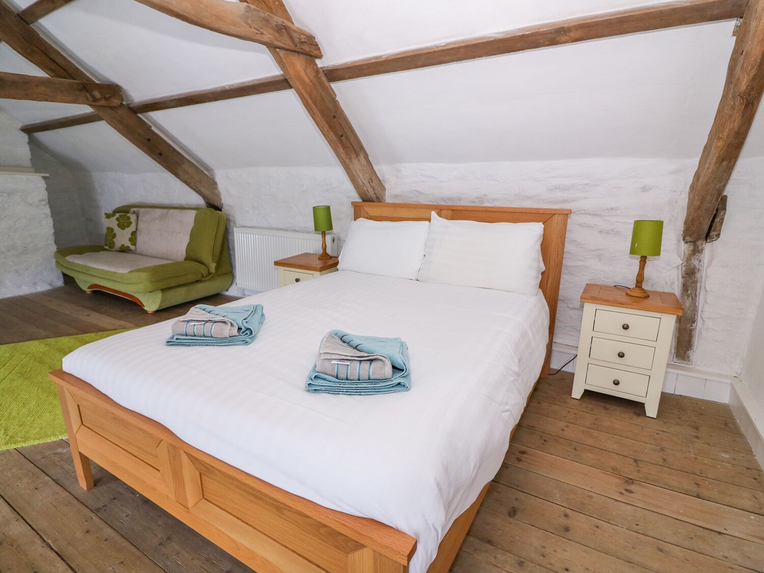 A bedroom with a wooden bed, a nightstand, a green chair, and a radiator.