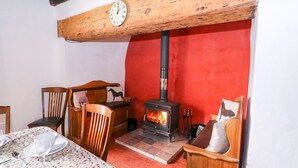 A cozy room with a wooden ceiling, a red wall, a wooden stove, and a clock. - Llwyncadfor Farm (Llandysul)