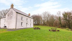A white building with multiple windows and a chimney, surrounded by a grassy area with picnic tables. - Llwyncadfor Farm (Llandysul)
