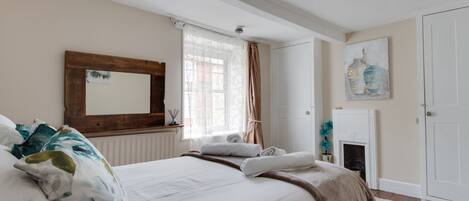 A bedroom with a bed, a mirror, a fireplace, and a window with curtains.