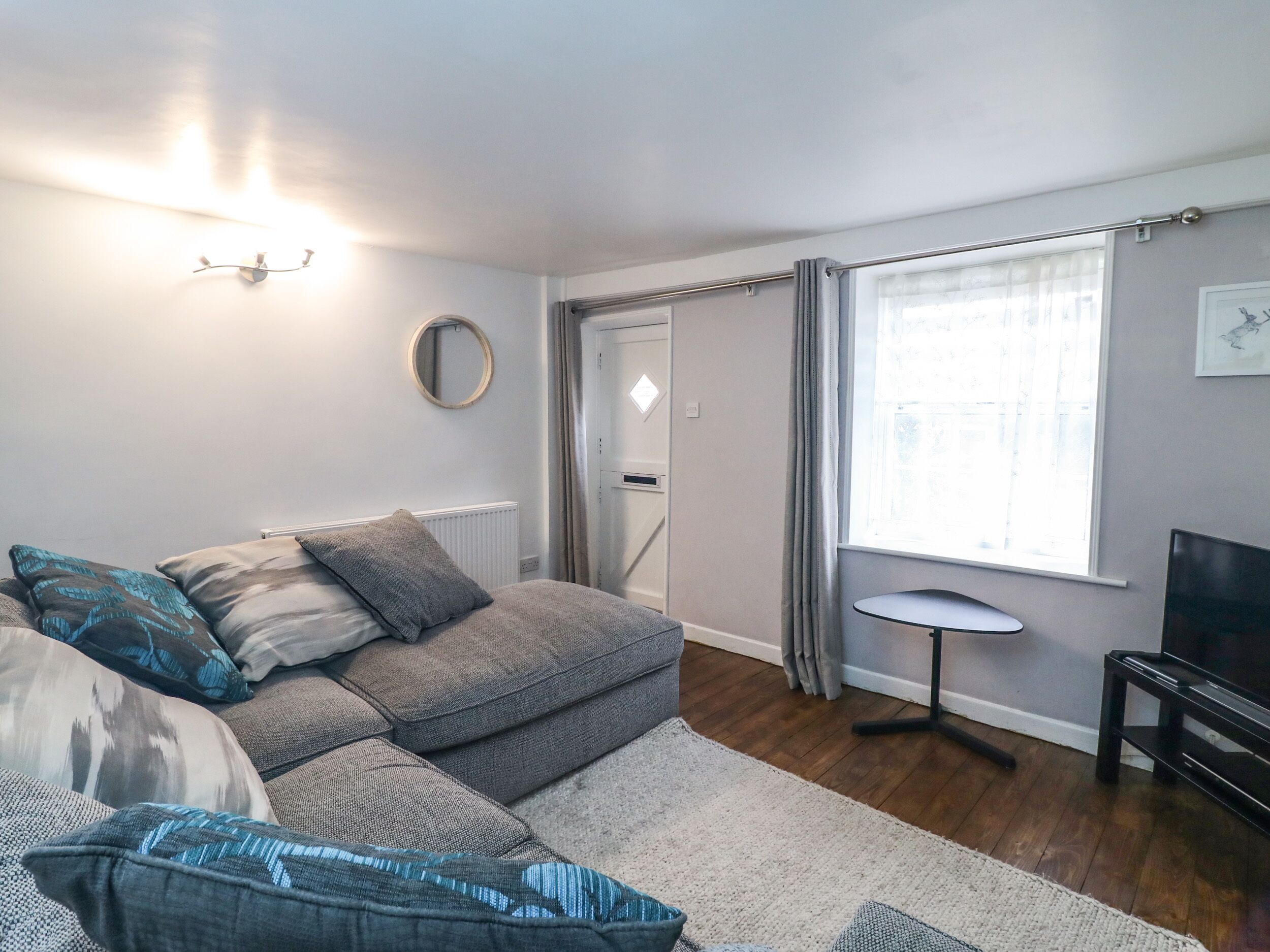 A modern living room with a grey sofa, a small round mirror, a round table, and a TV.