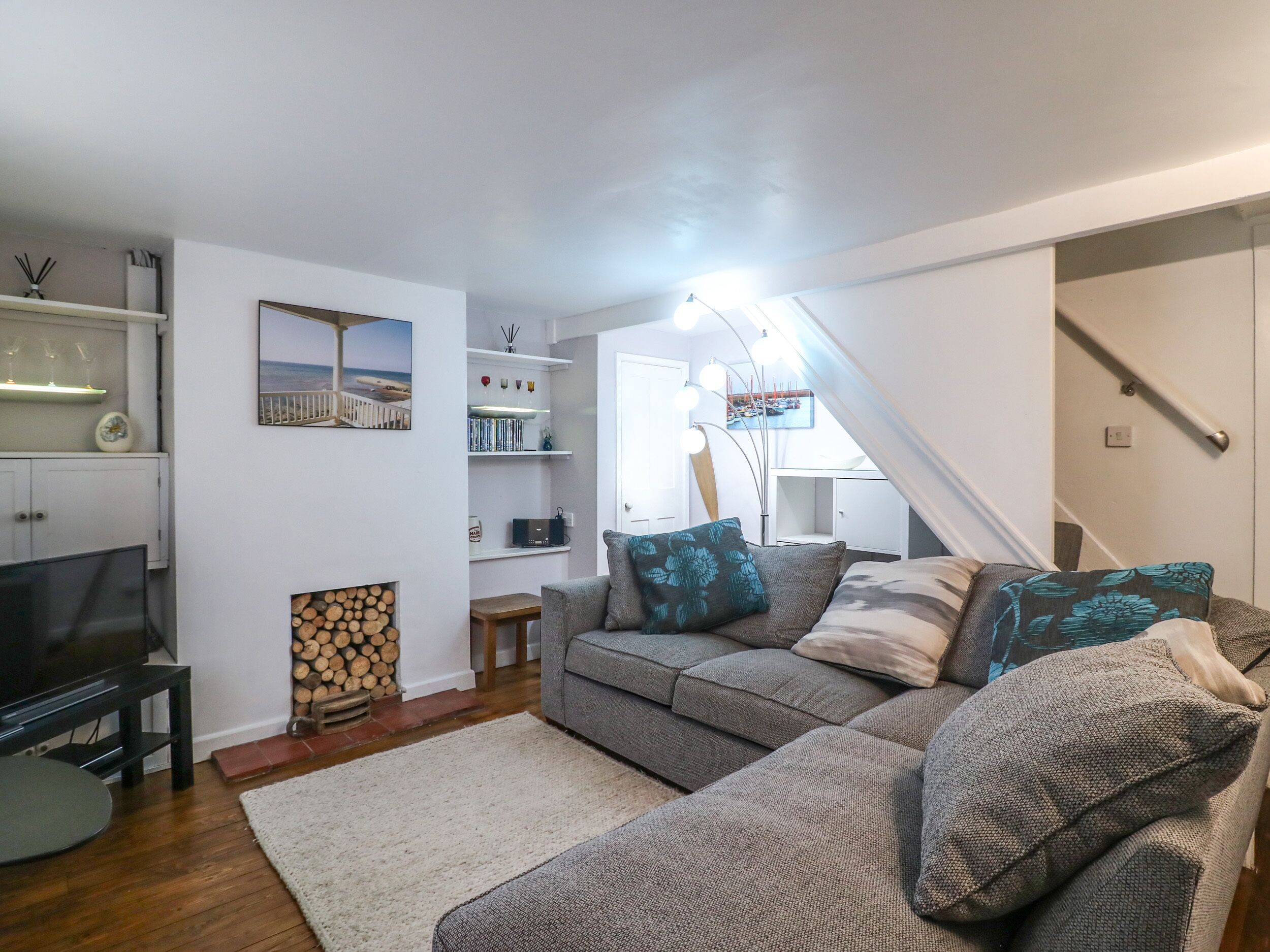 A living room with a grey sofa, a flat-screen TV, a fireplace, and a staircase.