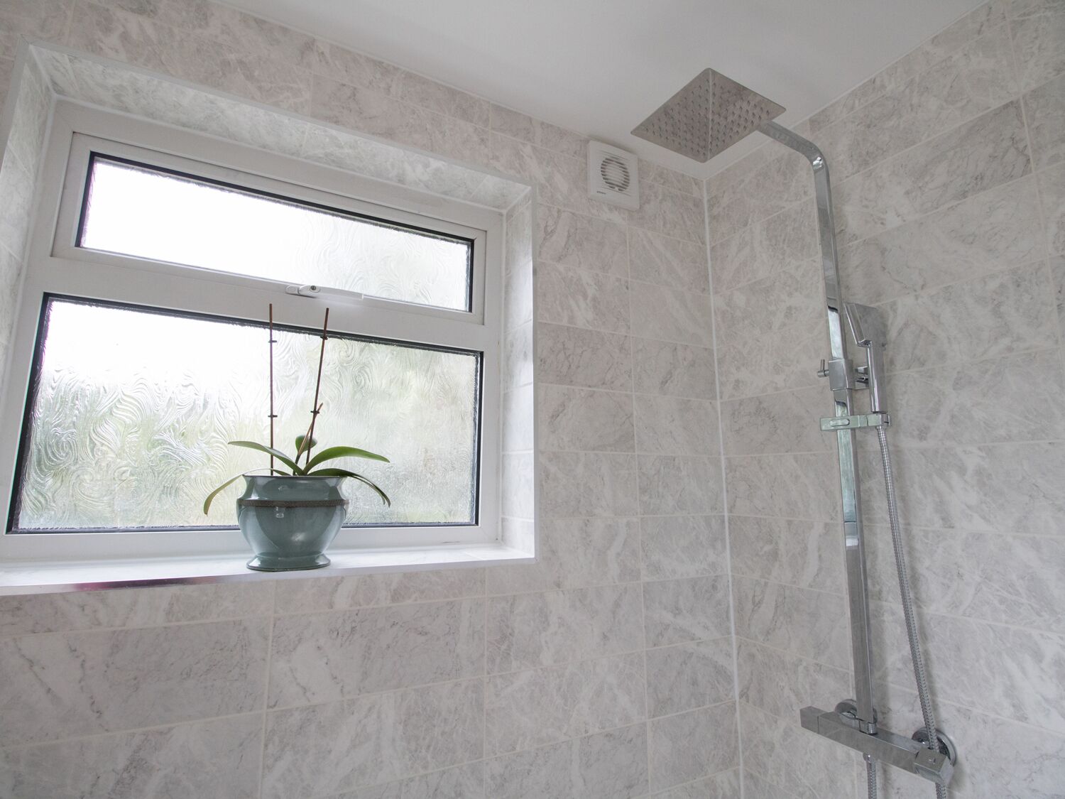 A bathroom with a shower, a window with a plant, and marble tiles.