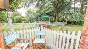 Un espace patio agrémenté d’une clôture en bois peinte en blanc, de chaises en bois, d  ’une table et d’un parasol vert.