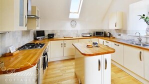 A modern kitchen with a wooden countertop, white cabinets, a built-in stove, and a skylight. - Fossil Barn (Weymouth)