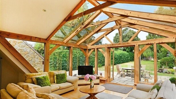 A cozy, open-plan living area with a wooden ceiling structure, a sofa set, a coffee table, and a TV. - Fossil Barn (Weymouth)