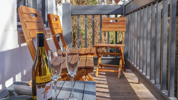 Un patio in legno con un tavolo, due sedie e una bottiglia di vino.