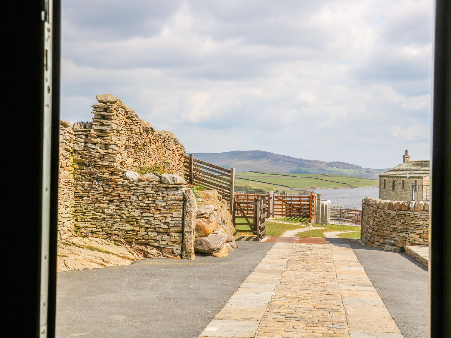 A stone pathway leading to a rustic stone wall and a wooden gate.